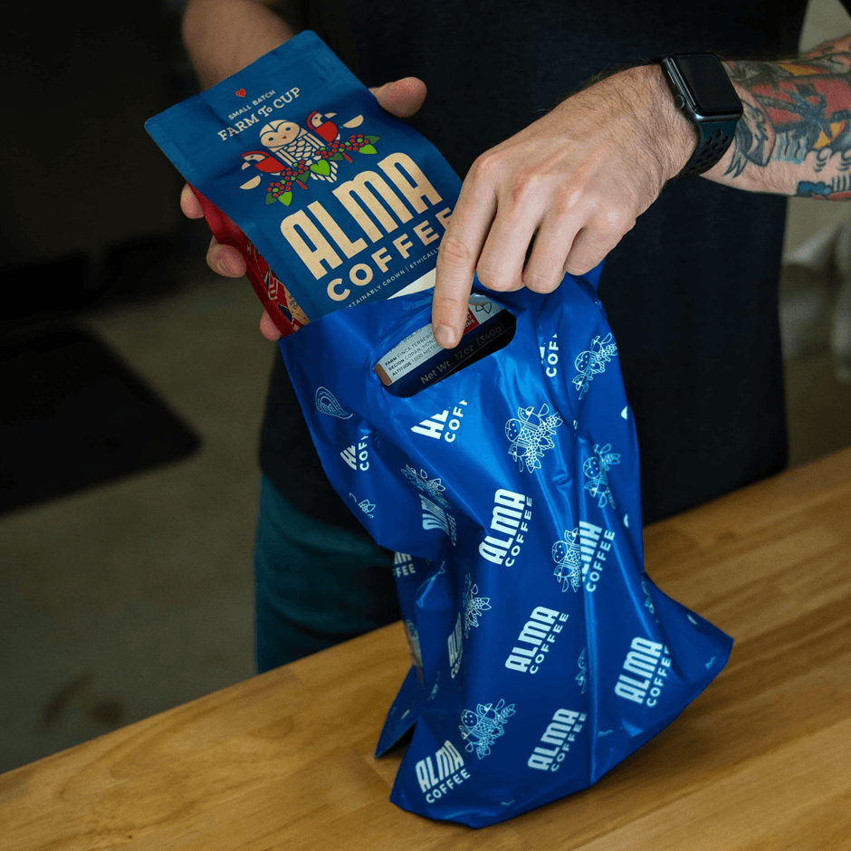 Alma Coffee’s blue die-cut handle bag being packed by a set of two hands.